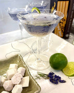 Cocktail in a martini glass with a lime and lavender garnish on a decorative plate.